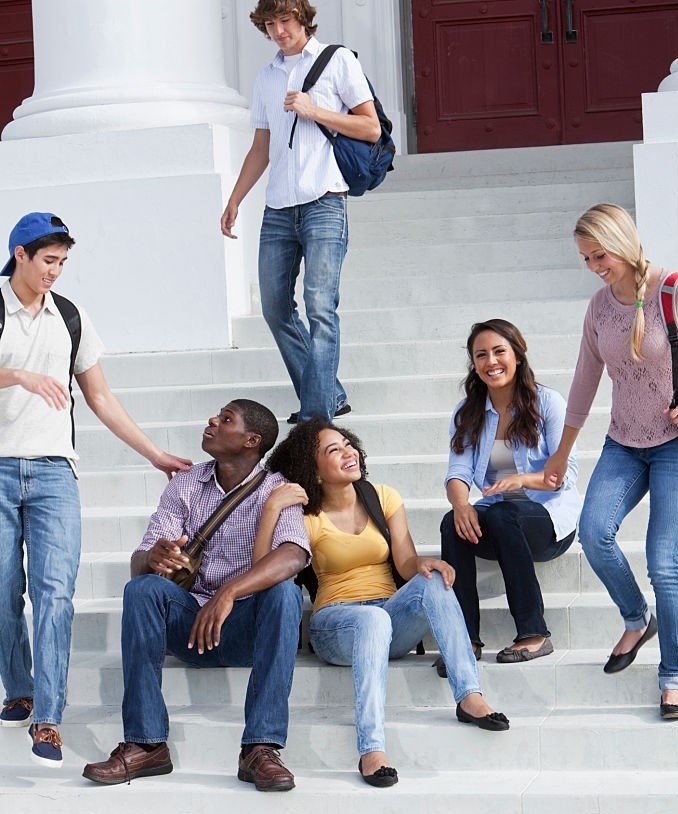 Multi-ethnic teenage students on steps of school building.